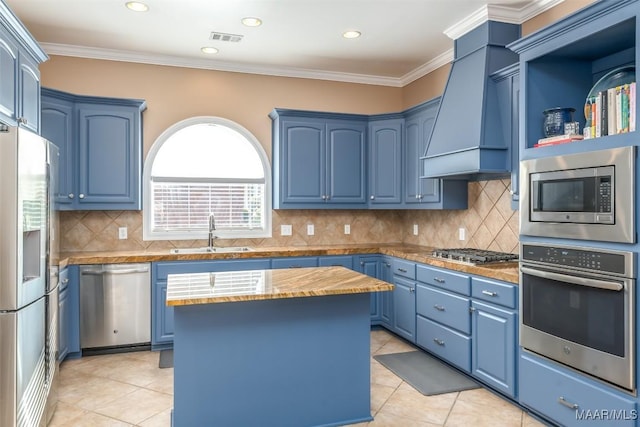 kitchen with a sink, custom range hood, blue cabinetry, and stainless steel appliances