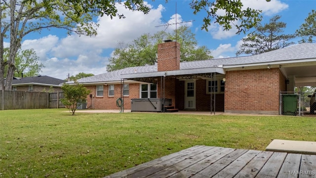 back of house with a chimney, brick siding, a hot tub, a yard, and fence