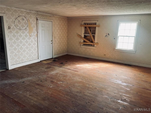 empty room featuring baseboards, hardwood / wood-style flooring, wallpapered walls, and a textured ceiling