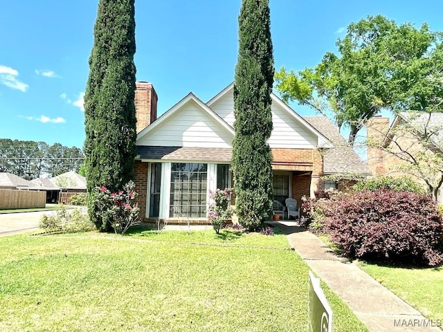 view of front facade featuring brick siding, a front yard, roof with shingles, and a chimney