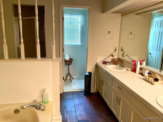 full bath with a sink, double vanity, wood finished floors, and a tub