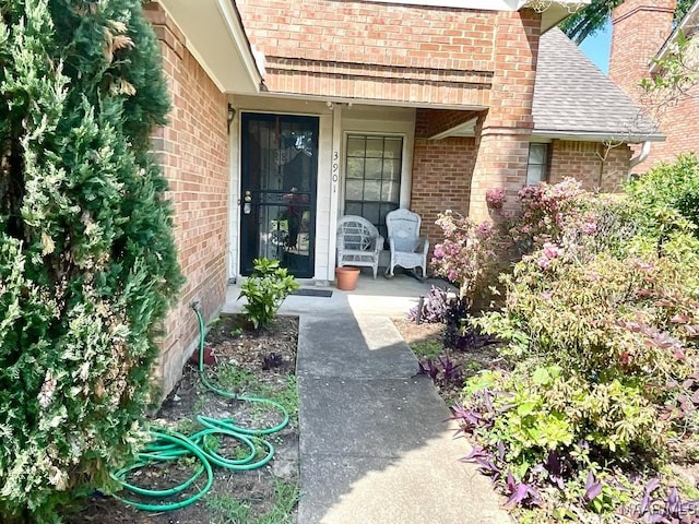 property entrance with a porch, a shingled roof, and brick siding
