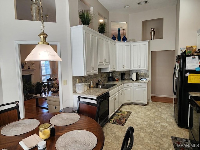 kitchen with a sink, black appliances, white cabinetry, a towering ceiling, and backsplash