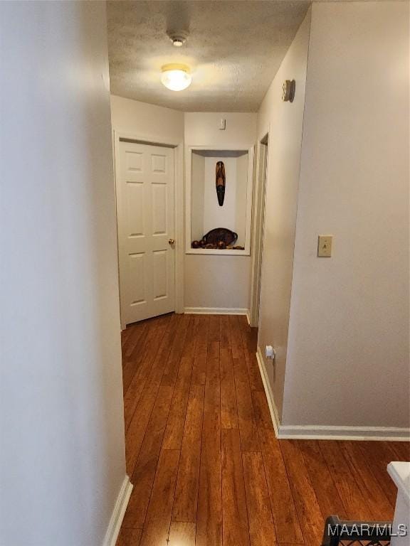 corridor featuring hardwood / wood-style flooring, baseboards, and a textured ceiling