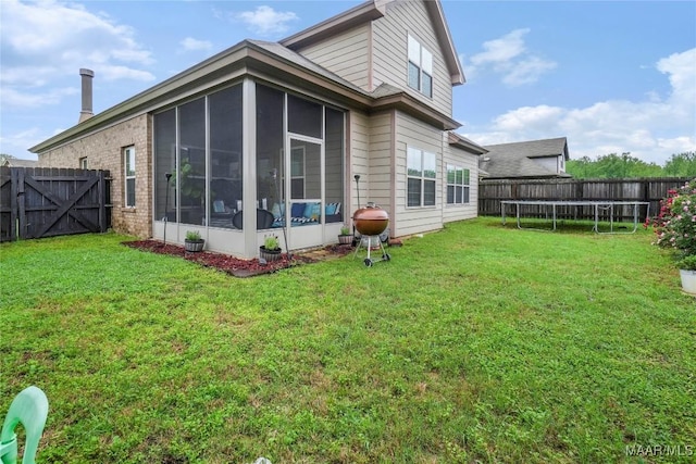 rear view of house featuring a yard, a fenced backyard, a trampoline, and a sunroom