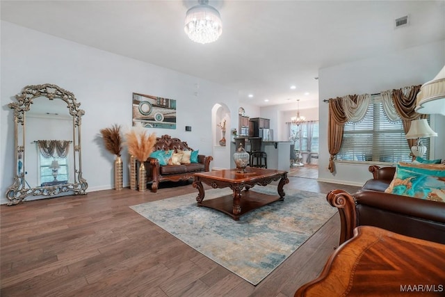 living area with visible vents, baseboards, arched walkways, an inviting chandelier, and wood finished floors