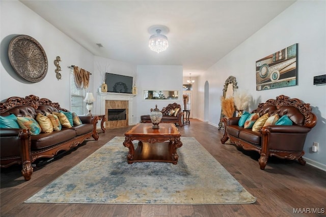 living room featuring a fireplace, arched walkways, wood finished floors, a notable chandelier, and baseboards
