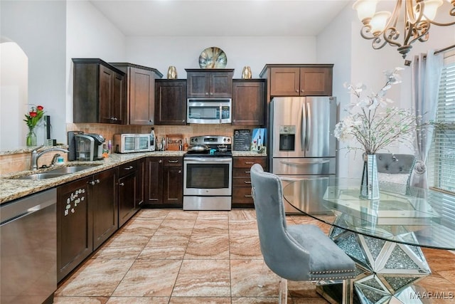 kitchen with an inviting chandelier, light stone countertops, a sink, stainless steel appliances, and backsplash