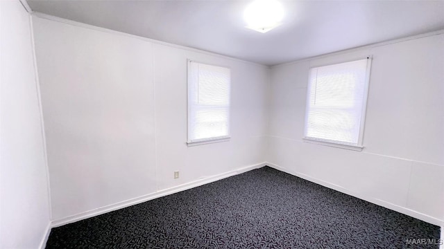 empty room featuring crown molding, baseboards, and dark colored carpet