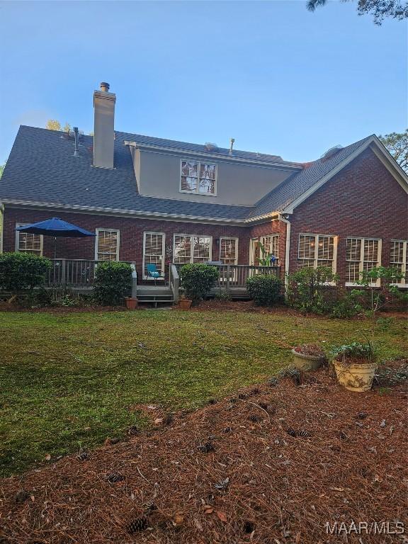 back of house featuring brick siding, a wooden deck, a lawn, and a chimney