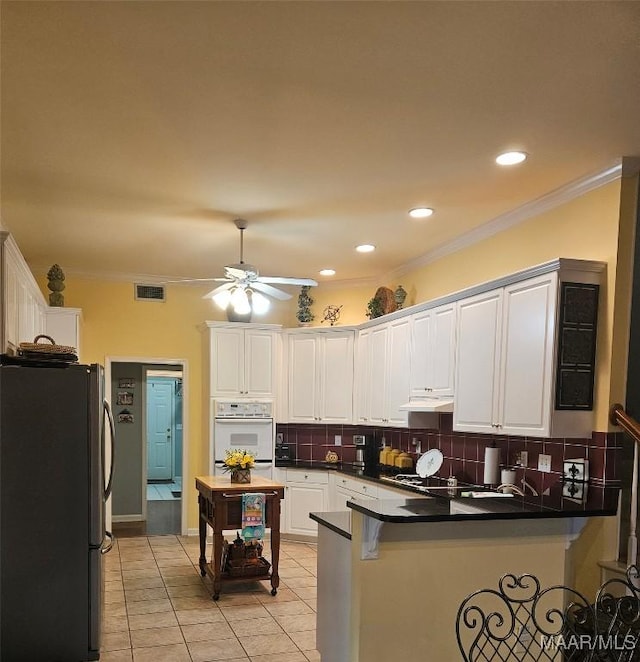 kitchen with freestanding refrigerator, ceiling fan, white oven, a peninsula, and visible vents