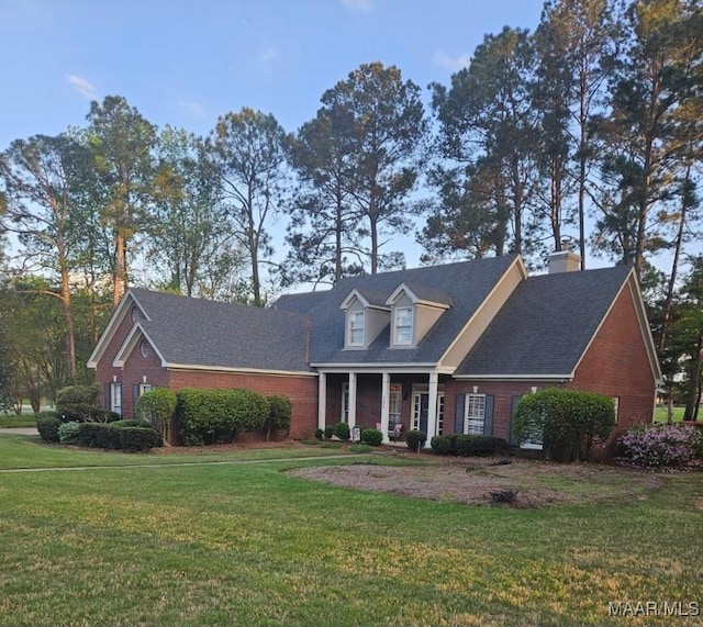 cape cod-style house featuring roof with shingles, a front yard, and brick siding