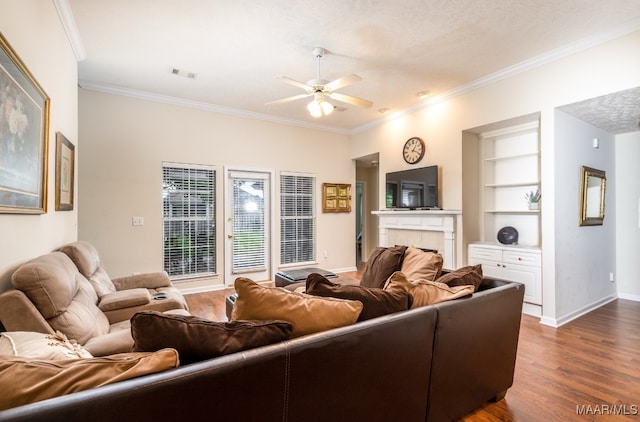 living room with visible vents, built in shelves, ceiling fan, dark wood finished floors, and crown molding