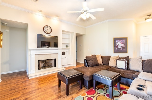 living room with built in features, ceiling fan, crown molding, and wood finished floors