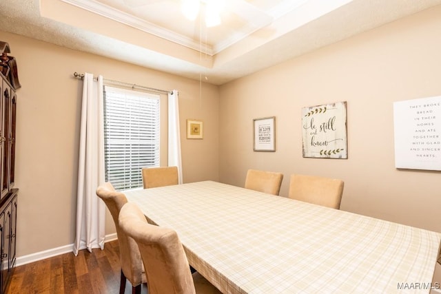 dining space with dark wood-type flooring, baseboards, a raised ceiling, and crown molding