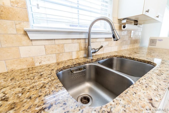 interior details featuring white cabinets, tasteful backsplash, a sink, and light stone counters