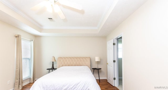 bedroom featuring ornamental molding, visible vents, a tray ceiling, ceiling fan, and wood finished floors