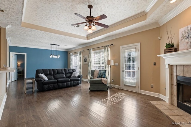 living area with a fireplace, a tray ceiling, a ceiling fan, and wood finished floors