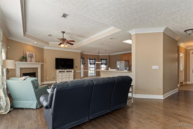 living area featuring visible vents, baseboards, a raised ceiling, ceiling fan with notable chandelier, and dark wood-type flooring