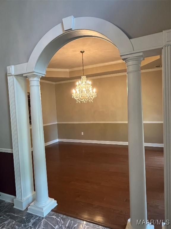 unfurnished dining area with wood finished floors, baseboards, arched walkways, and ornate columns