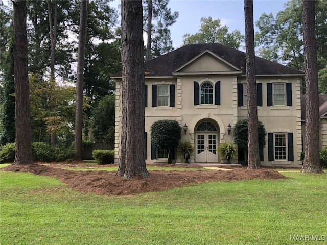 colonial inspired home with stucco siding, a front lawn, and french doors