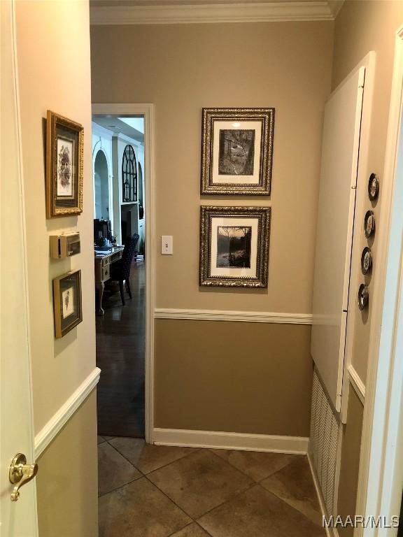 hall with dark tile patterned flooring, baseboards, and crown molding