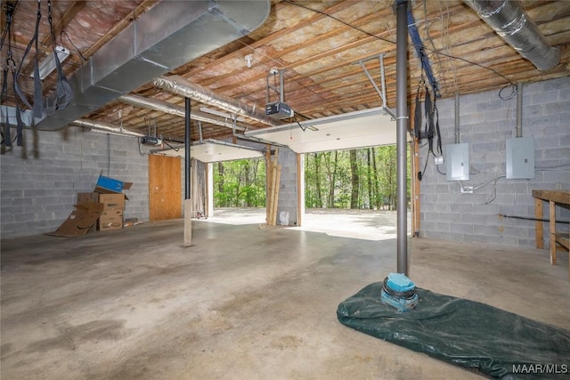 garage with a garage door opener, electric panel, and concrete block wall