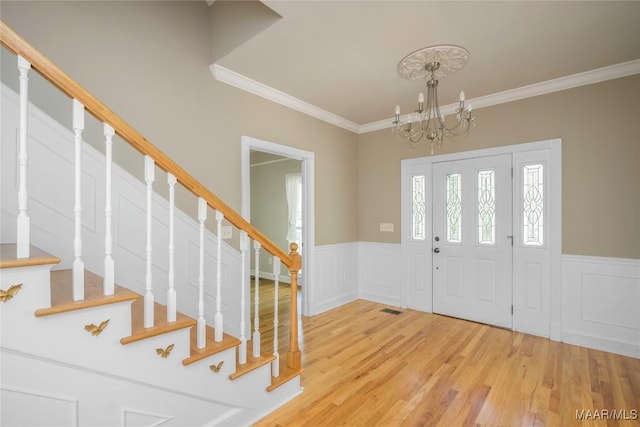 foyer featuring light wood-style floors, ornamental molding, a wainscoted wall, and stairway