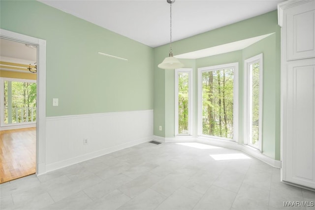 unfurnished dining area with wainscoting, baseboards, and visible vents