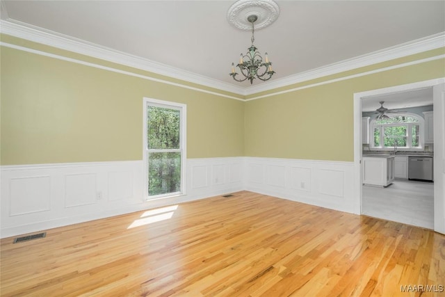 spare room featuring an inviting chandelier, light wood-style flooring, ornamental molding, visible vents, and wainscoting