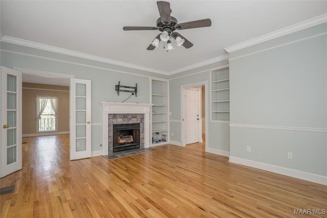 unfurnished living room with built in features, baseboards, a tiled fireplace, crown molding, and light wood-style flooring