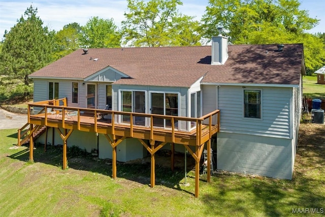 rear view of house featuring a shingled roof, a wooden deck, a chimney, and a lawn