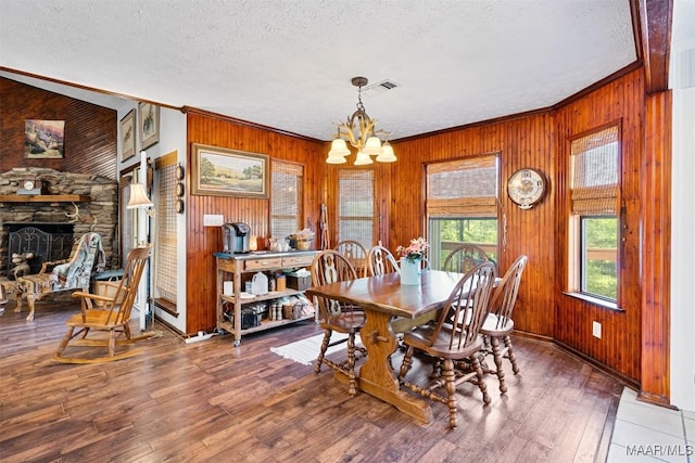 dining room featuring crown molding, an inviting chandelier, a textured ceiling, wood finished floors, and wooden walls