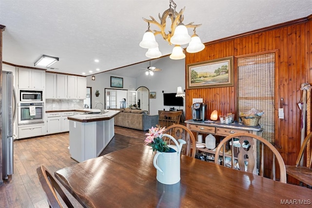 dining space featuring wood walls, ceiling fan with notable chandelier, crown molding, and a textured ceiling