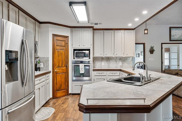 kitchen featuring a sink, appliances with stainless steel finishes, light wood-style floors, a peninsula, and decorative backsplash