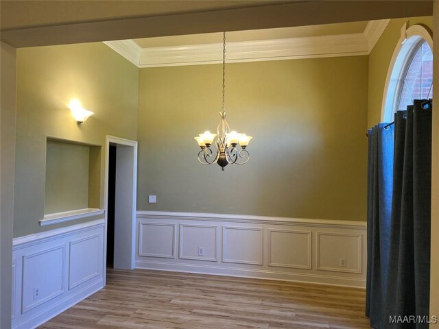unfurnished dining area featuring a chandelier, crown molding, wainscoting, and light wood-style floors