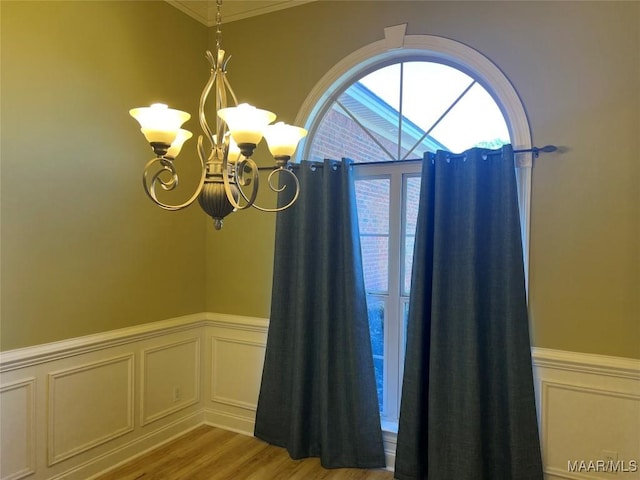 details featuring a decorative wall, a wainscoted wall, a chandelier, and wood finished floors