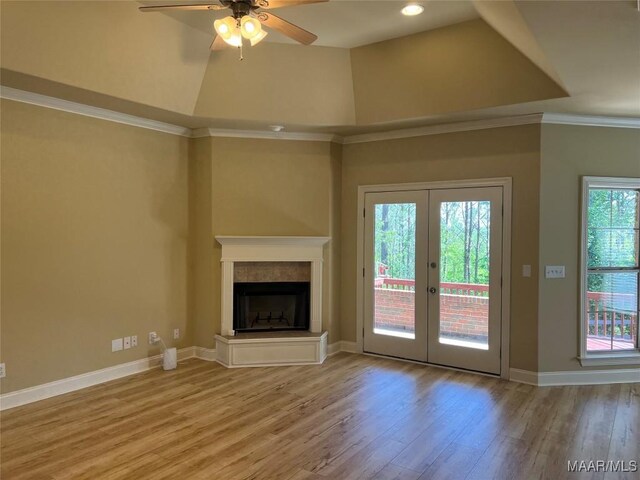 unfurnished living room featuring baseboards, french doors, a ceiling fan, a fireplace with raised hearth, and wood finished floors