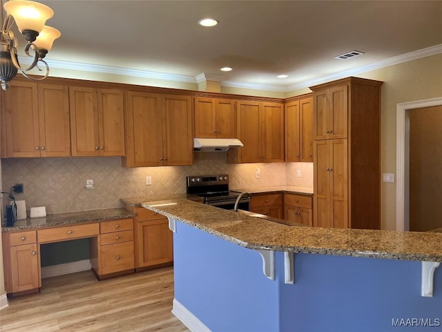 kitchen featuring ornamental molding, under cabinet range hood, a kitchen bar, brown cabinetry, and electric stove