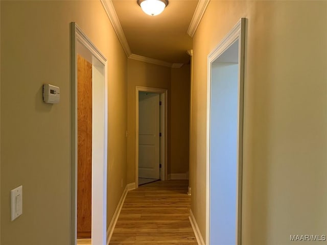 corridor featuring crown molding, baseboards, and light wood-style floors