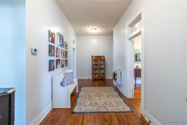 hall with a textured ceiling, wood finished floors, baseboards, and heating unit