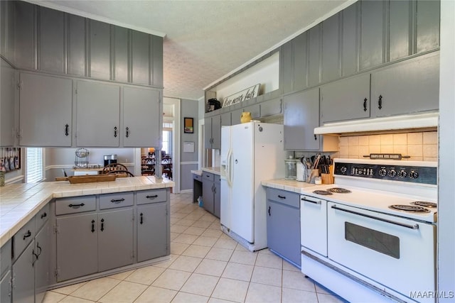 kitchen with a textured ceiling, under cabinet range hood, tile counters, and white appliances