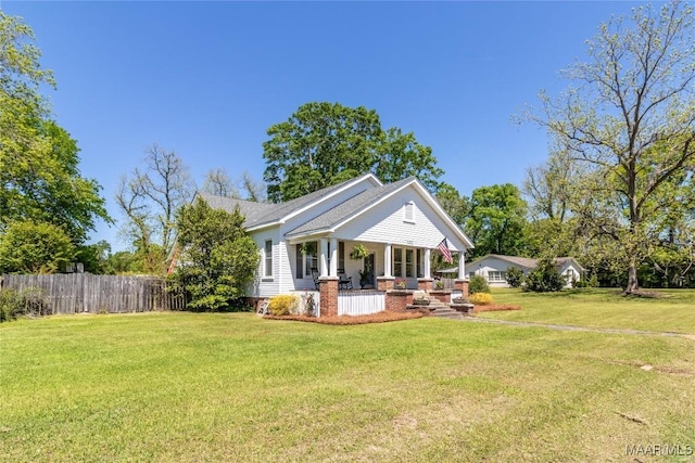 rear view of property featuring a yard, fence, a shingled roof, and covered porch