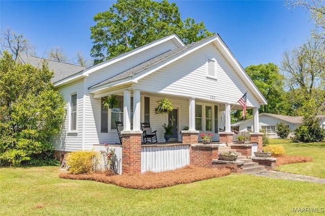 rear view of house featuring roof with shingles, covered porch, and a lawn