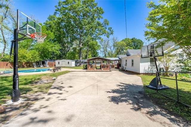 view of basketball court with a storage shed, fence, a fenced in pool, and a yard