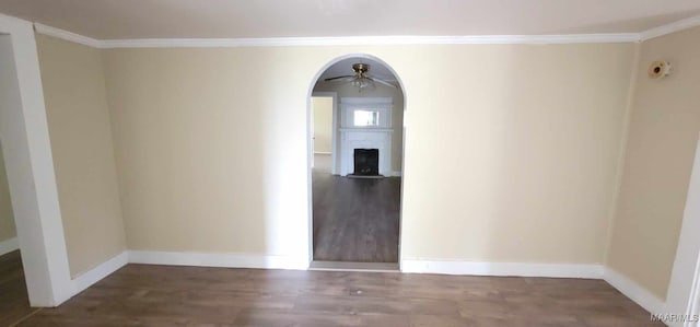 spare room featuring baseboards, a fireplace with flush hearth, ceiling fan, arched walkways, and wood finished floors
