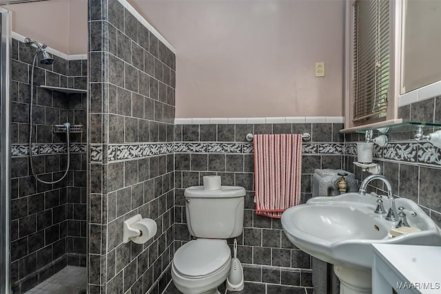 full bathroom featuring a sink, tile walls, toilet, a walk in shower, and wainscoting