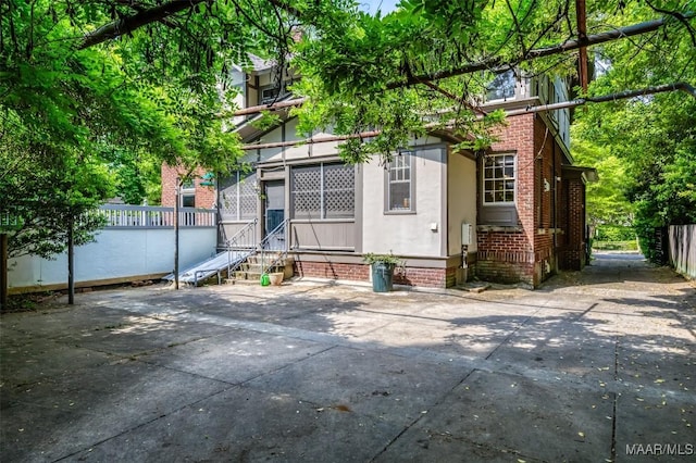 rear view of house with brick siding, entry steps, fence, and stucco siding