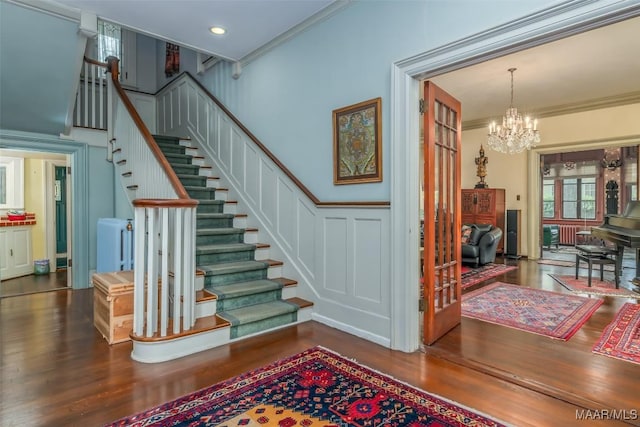 stairs with a decorative wall, ornamental molding, a notable chandelier, and wood finished floors