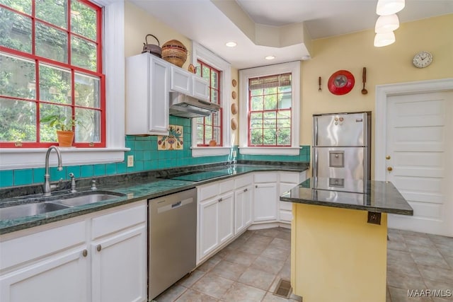 kitchen with dark stone countertops, white cabinets, under cabinet range hood, stainless steel appliances, and a sink
